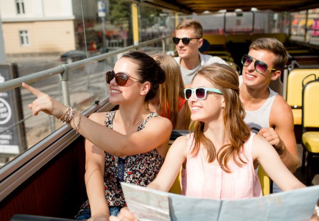 group of smiling friends traveling by tour bus